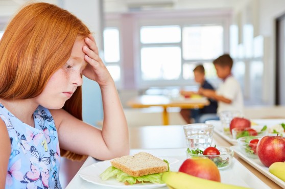 Niña triste delante de un plato en un comedor escolar